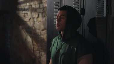 Kapüşonlu kararlı boksör duvara yaslanıyor ve maçtan önce dikkatini topluyor. Gölgeler ve dokular yoğun atmosfer yaratır. Zihinsel ve fiziksel hazırlık kavramı