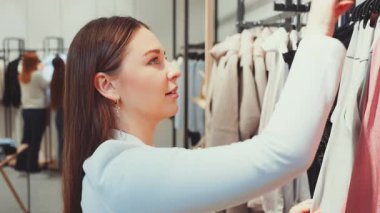 Bir moda mağazasında alışveriş yaparken elinde pembe bir bluz tutan kadın elbiseyi incelerken gülümsüyor. Alışveriş, moda, perakende terapi ve yeni kıyafetler seçerken keyif alma kavramı