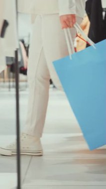 Beyaz pantolon ve spor ayakkabı giyen bir kişi bir perakende mağazasında yakalanan büyük mavi bir alışveriş çantasını elinde tutarak içeri girer.