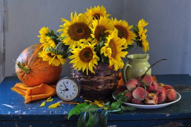 Bahçedeki ahşap bir masada kırmızı ve yeşil ayçiçeği ve şeftali demeti..