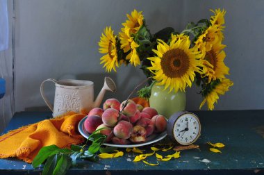 Bahçedeki ahşap bir masada kırmızı ve yeşil ayçiçeği ve şeftali demeti..