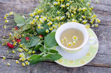 Tahta arka planda papatya çiçekleri olan bir fincan çay. 