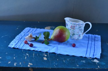 Taze kırmızı erikli bir fincan ve beyaz ahşap bir masada mavi bir elma..