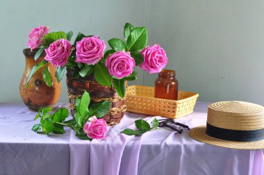 Kafedeki masasında hasır şapka olan vazoda pembe güller ve şapka..