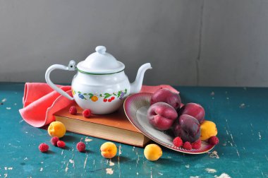 Tabaktaki taze meyve ve sebzeler bir kitap ve bir fincanla birlikte.