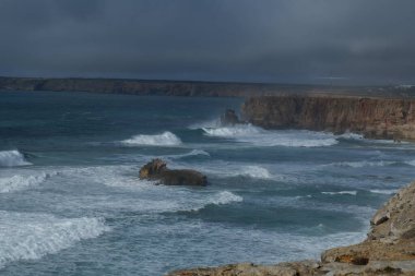 Güzel bulutlu bir gökyüzü ile kayalık bir sahilin dikey görüntüsü