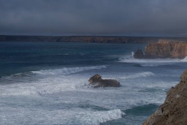 Bulutlu arka planda bir kayayla güzel bir deniz görüntüsü.