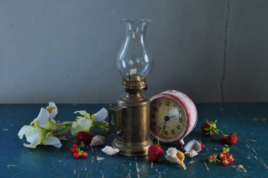 Mumla dolu bir hayat. Klasik saat, bir buket kırmızı çilek, çiçekler, cam vazo, klasik lamba ve eski cam sürahi