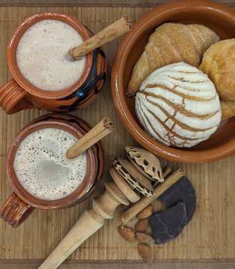 Meksika ekmeği, çikolata parçaları ve içki. Ahşap havan, tarçın çubukları ve arkaplanda badem. Kil çanak çömlek