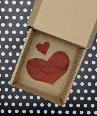 Siyah beyaz noktalı arka planda, karton kutuda iki kırmızı kağıt kalp.