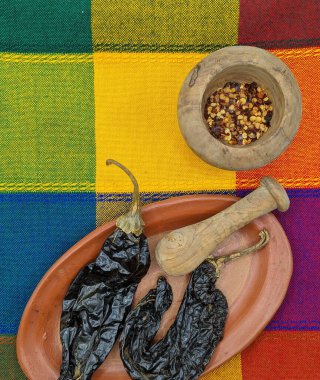 Kil tabakta Meksika kuru biberleri, ahşap havan ve geleneksel renkli kareli masa örtüsünde taban.