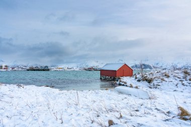 Kuzey Atlantik kıyısındaki ilginç bir ev sabah ışıklarıyla. Hillesy ve Sommary 'nin karlı adalarındaki renkli tatil evleri. Göl kenarındaki kırmızı ev. Troms, Kuzey Norveç 'te Tatil