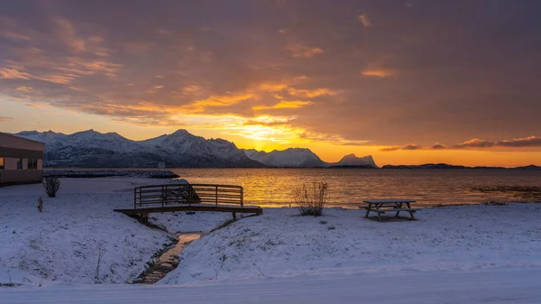 ノルウェーのセンジャの雪の山の上に明るい日差しでアフターグロー 赤い雲はスカーランドのフィヨルドの水に反射しています ベルクシアンを望むベルクスフィヨルデンの夕日 — ストック写真