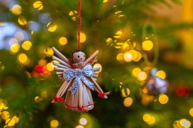 Gümüş kurdeleli güzel bir saman meleği Noel ağacının çam dalına asılı, aydınlanmış Noel süslemelerinin ortasında, yeşil Noel ağacında