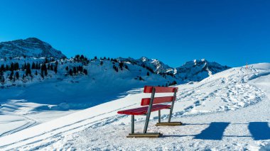 Arlberg, Vorarlberg, Avusturya 'dan gelen karlı dağlara ilginç panoramik manzaralı kırmızı park bankı