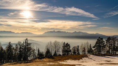 Güneş, Ren Vadisi 'nin üzerinde, Feldkirch şehrinde güneş ışınlarıyla ağaçları, çayırları ve tarlaları aydınlatıyor. Arka planda İsviçre dağları ve gökyüzünde ilginç renkli bulutlar var.