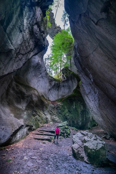 Woman in a cave that is open at the top and lets light in through the crack, overgrown with plants. The Kirchle near Dornbirn is a fairytale place, hidden in the forest on a hill. Boulders and moss lie in it