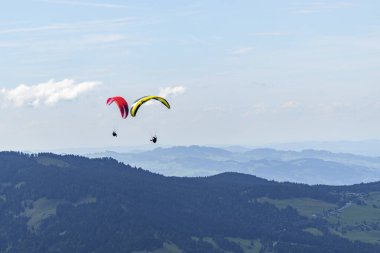 Mavi bulutlu gökyüzünde paraşüt broşürleri, yeşil çayır, köknar ağacı, mavi su ve dağ sırasıyla Constance Gölü üzerinde paraşüt manzarası. Bregenz Ormanı, Vorarlberg 'de yaz günü,
