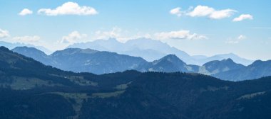 Bregenzerwald panoramasında dağ siluetleri ve arka planda Sntis var. Gün batımı kırmızı ve sisli hatları görünür kılar..