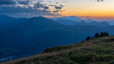Bregenzerwald panoramasında dağ siluetleri ve arka planda Sntis var. Gün batımı kırmızı ve sisli hatları görünür kılar..