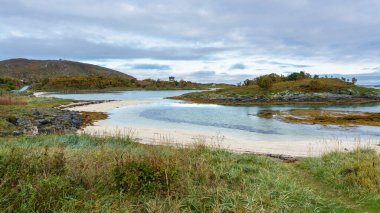 Sommarya, Troms, Norveç 'te taşlarla, yosunlarla ve beyaz kumlarla çevrili mavi turkuaz laguna. Arka planda tatil evi ve dağ var. Macera için özel bir yer  