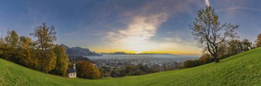 Panorama Sunset in the Rhine Valley, with a tree and a chapel,blue sky over the city of Dornbirn, meadow and fields. with Swiss mountains in the background. afterglow, interesting colored veil clouds clipart