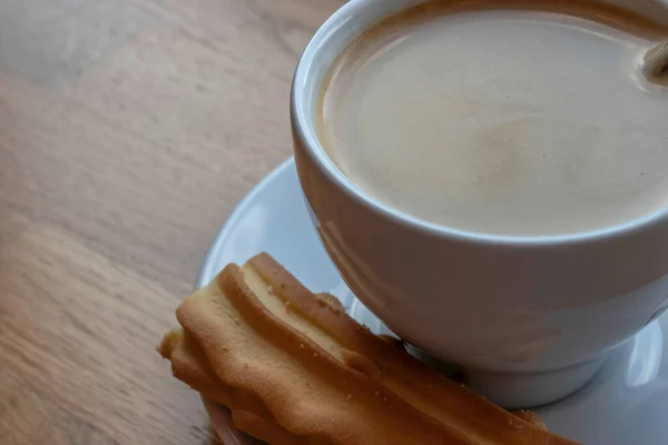柔らかいビスケットと一緒に木製のテーブルの上に置かれたカプチーノの蒸しカップを示すトップビューの画像 暖かいコーヒーを飲みながら美味しいビスケットを味わうという楽しい体験ができます — ストック写真