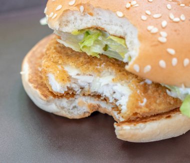 Taze marulla kaplanmış tavuk burgeri, göz kamaştırıcı bir siyah gölgeye karşı servis ediliyor. Görsel bir zevk ve seçilmiş bir odak.