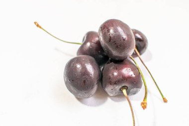 Koyu Kırmızı Kiraz: Saf beyaz bir yüzeyde koyu kırmızı bir kiraz içeren gerçek bir fotoğraf, basit ama güçlü bir görsel karşıtlık yaratır. - Stok fotoğrafları..