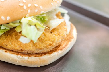 Taze marulla kaplanmış tavuk burgeri, göz kamaştırıcı bir siyah gölgeye karşı servis ediliyor. Görsel bir zevk ve seçilmiş bir odak.