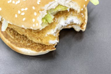 Taze marulla kaplanmış tavuk burgeri, göz kamaştırıcı bir siyah gölgeye karşı servis ediliyor. Görsel bir zevk ve seçilmiş bir odak.