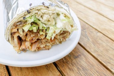 Tavuk Shawarma Paketi: Ağzını sulandıran bir Shawarma Doner kebabı, tavukla sarılmış, yanında sos ve sebzelerle birlikte beyaz bir tabakta servis ediliyor..