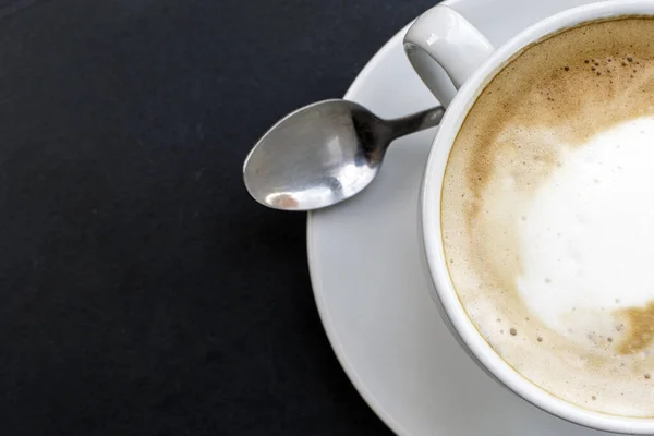 Hot Cappuccino: Experience the warmth of a freshly brewed cappuccino in a charming white cup, beautifully arranged on a table, viewed from the top.