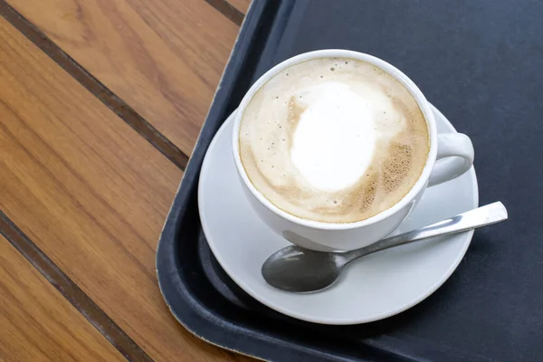Hot Cappuccino: Experience the warmth of a freshly brewed cappuccino in a charming white cup, beautifully arranged on a table, viewed from the top.