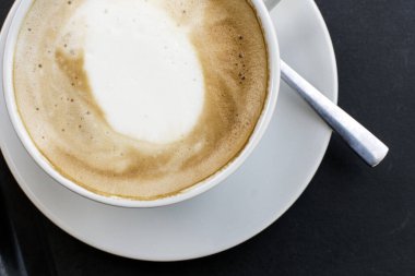 Sıcak Cappuccino: Yeni demlenmiş bir kapuçinonun sıcaklığını en üstten bakıldığında güzel bir şekilde bir masanın üzerinde duran büyüleyici beyaz bir bardakta deneyimleyin..