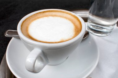 Sıcak Cappuccino: Yeni demlenmiş bir kapuçinonun sıcaklığını en üstten bakıldığında güzel bir şekilde bir masanın üzerinde duran büyüleyici beyaz bir bardakta deneyimleyin..