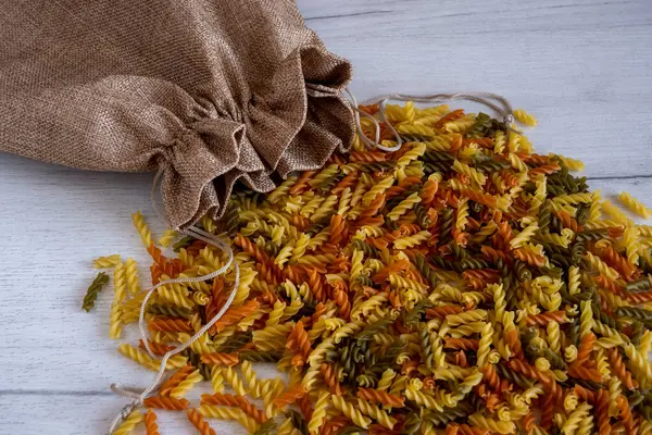 Pişmemiş çok renkli Fusilli makarnası beyaz ahşap arka plandan dökülüyordu. Üst Manzara. Yüksek kalite fotoğraf