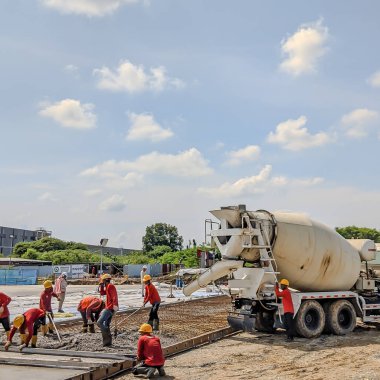 İnşaat alanındaki işçiler mikser kamyonunun kalıbına beton döküyorlar. İşçiler yol inşaatına mikser kamyonundan taze beton döküyorlar..