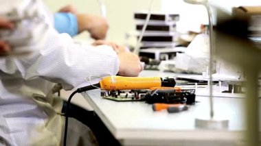 Teknoloji fabrikası işçileri seçilen yedek parçalardan elektronik ürünler monte ediyorlar. Elektronik fabrikasının arka planında devre tahtaları var.