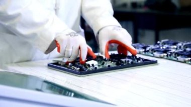 Teknoloji fabrikası işçileri seçilen yedek parçalardan elektronik ürünler monte ediyorlar. Elektronik fabrikasının arka planında devre tahtaları var.