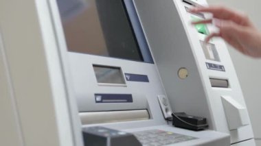 Yakından bakınca, kredi kartını ATM makinesine sokuyor. ATM bankadan para çekiyor.