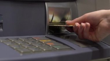 Yakından bakınca, kredi kartını ATM makinesine sokuyor. ATM bankadan para çekiyor.