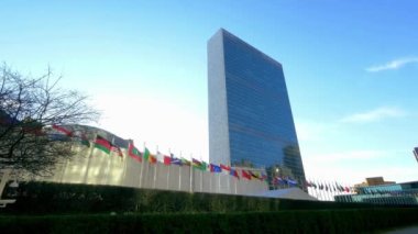 Mavi gökyüzü altında birçok ülke bayrağı bulunan kurumsal binaların altından gökdelenler.