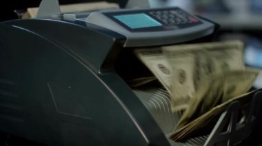 Para sayma makinesi dolar sayıyor. Makineden geçen 100 dolarlık banknotlar fatura sayma makinası konseptini kullanarak yatırım yapıyor.