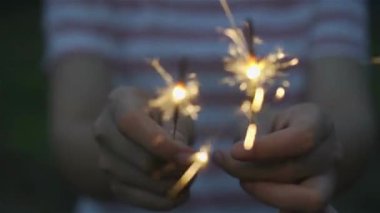 El ele tutuşan, arka planda bulanık havai fişek patlaması parti havai fişekleri bayramı kutlaması.