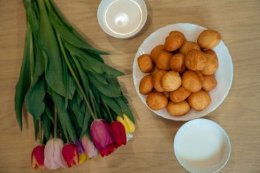 Bir fincan çay, bir buket lale ve bir bardak sütle ahşap bir masada.