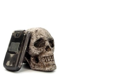 Metal bir kafatası üzerinde dinlenen eski bir cep telefonu, konsept mesaj ve sürüş tehlikeli