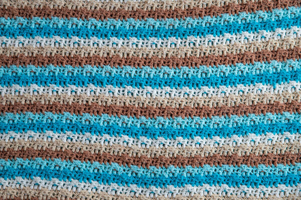 крупным планом бабушкиного вязанного голубого, загара, коричневого и белого полосатого одеяла, это одеяло заставляет вас думать о бабушкином доме, он уютный и теплый, отлично подходит для больничных дней, холодного зимнего утра, и ленивые дни на диване.