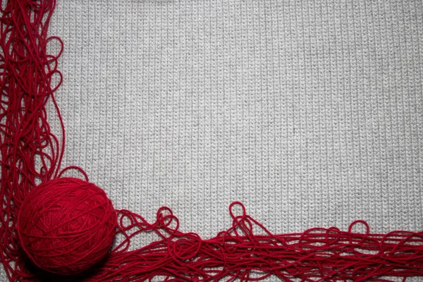 gray knitted or crocheted tight knit blanket with a red yarn edging and a ball of yarn, close up top view of crocheted gray background with red yarn border with a place for text, for yarn and crafting hobby related needs with copy space with ball of
