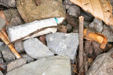 close up of gravel, stones, and sticks with a used old cigarette butt littered in it. Top view. 